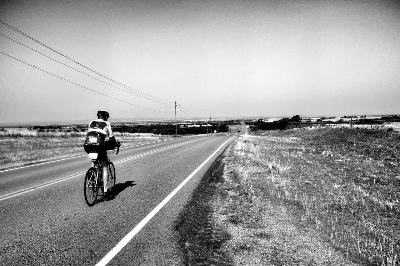 B&W photo of a cyclist headed down a paved higway.