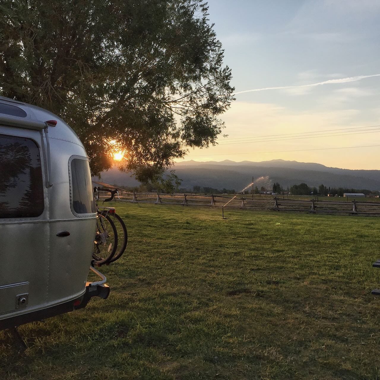 Color photo of Airstream trailer in a green field with sprinklers running in the background.